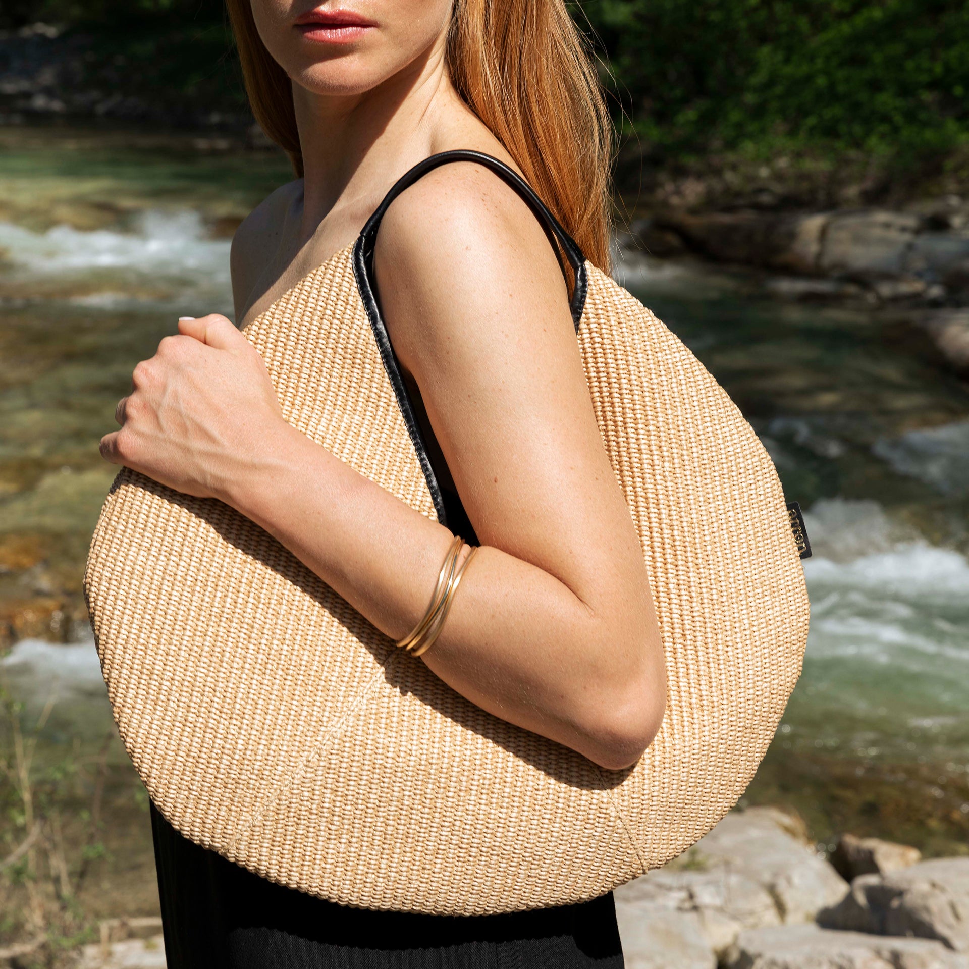 Borsa hobo rotonda in rafia naturale e pelle nera design minimale e contemporaneo indossata lifestyle